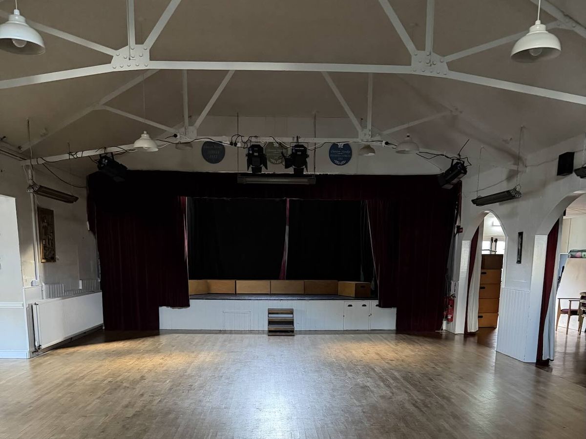 The main hall with its sprung wooden floor, looking towards the stage with red curtains and stage lights